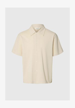 Chemise beige à manches courtes avec boutons, col pointu, tissu lisse et étiquette de marque "Selected" à l'intérieur de l'encolure.