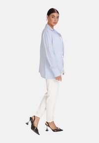 Camicia button-up azzurra chiaro con maniche lunghe, tessuto testurizzato, abbinata a pantaloni bianchi aderenti e scarpe con tacco nere con dettaglio a fiocco.