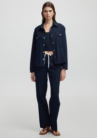 Marineblauwe cropped jack met twee borstzakken en drukknoopsluitingen, gecombineerd met een bijpassende cropped top en recht gesneden broek. Gladde stof.