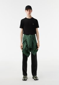 Camiseta negra con logo, joggers verdes atados a la cintura, pantalones negros y zapatillas multicolores. Look deportivo simple y casual.