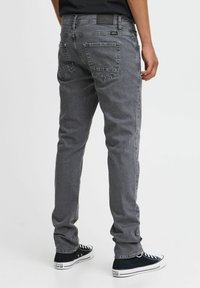 Grijze denim jeans met een slim fit, vijf zakkenontwerp en zichtbare stiksels op de zakken, gecombineerd met zwarte hoge sneakers.