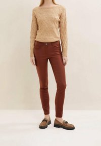 Beige svetr z pleteniny s širokým výstřihem, spárovaný s úzkými džíny v hnědé barvě a hnědými mokasíny s černými akcenty.