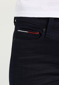 Los pantalones vaqueros de mezclilla azul marino cuentan con un pequeño bolsillo frontal con acentos de costura en rojo, blanco y azul, y un diseño clásico de cinco bolsillos.