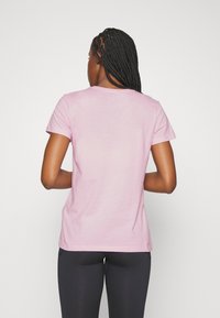 Rosa bomullst-shirt med korta ärmar, rund halsringning och slät textur, bärs med svarta sportbyxor.