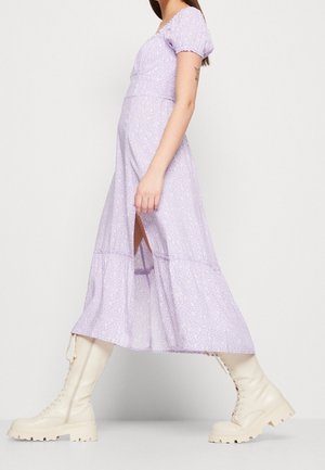 Robe longue lavande à motif floral, manches bouffantes courtes et ourlet à volants. Portée avec des bottes crème montantes jusqu'aux genoux, dotées d'une semelle épaisse.