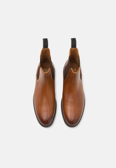 Botas de tornozelo em pele castanha com painéis laterais elásticos, laços para puxar e bico arredondado. Textura suave e detalhes contrastantes em preto.