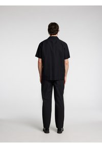 Maglietta nera a maniche corte con colletto classico, abbinata a pantaloni neri coordinati. Design semplice, realizzata in un tessuto leggero e liscio.