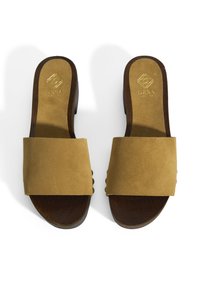 Bruine suede slide-sandalen met brede banden. Houten hak en binnenzool. Textuurdetail op de banden met een zachte afwerking. Gouden branding op de binnenzool.