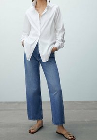 White button-up shirt, relaxed fit with rolled sleeves, paired with high-waisted blue jeans, straight-leg cut, and beige sandals.