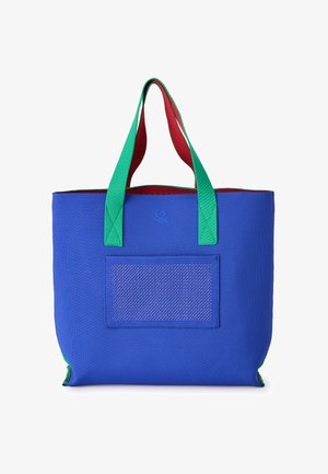 Blaue Tragetasche mit grünen Griffen und rotem Innenfutter, mit einer vorderen Netz-Tasche und kleinem, geprägtem Logo im oberen Zentrum.