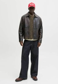 Ruda odinė striukė virš tekstūruoto rudo megztinio, derinama su laisvais tamsiais džinsais ir rudais batais. Raudona kepurė su balta iškarpa.