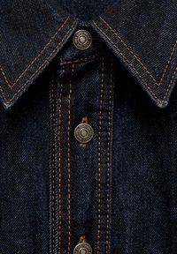 Col montant en denim bleu foncé avec des coutures orange et des boutons-pression en métal portant l'inscription "Est. 1981 GWNJ JEANS."