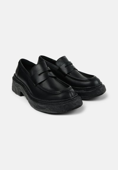 Black leather loafers with a raised, textured sole, featuring a smooth upper and strap detailing across the front.