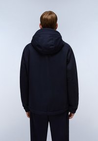 Chaqueta acolchada de color azul marino con capucha, diseñada con una textura suave y puños elásticos, mostrada desde la parte posterior sobre un fondo claro.