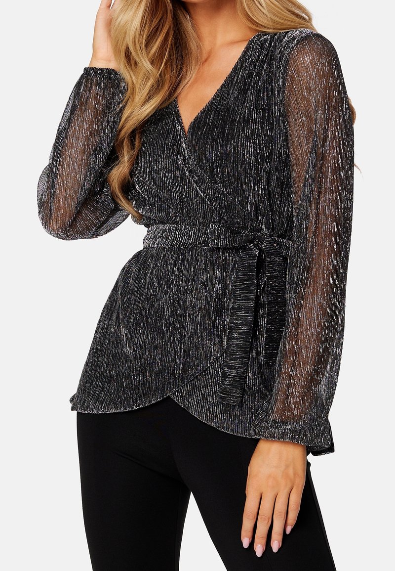Top negro envolvente confeccionado con una tela brillante, que presenta mangas largas y transparentes, una cinturilla con lazo y un dobladillo curvado. Texturizado con detalles de hilo metálico.