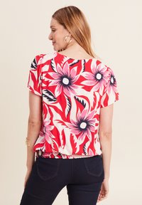 Blümchenoberteil mit einem rot, pink und weißen Design, kurzen Ärmeln und gerüschtem Taillendetail. Glattes Material mit auffälligen Blumenmustern.