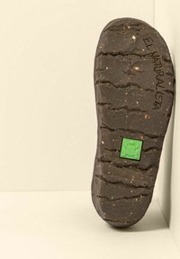 Suola di scarpa in gomma naturale, texture con profonde scanalature e un emblema di rana in verde. Il colore è marrone scuro con piccoli dettagli maculati.