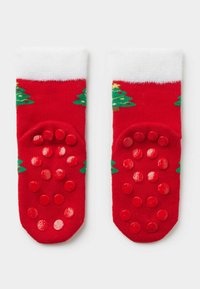 Červené bavlněné ponožky s bílým lemem, zdobené vzory vánočního stromečku v zelené barvě. Spodní část má červené gumové tečky pro lepší přilnavost.