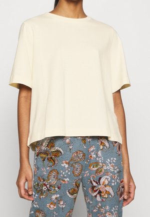Kortærmet t-shirt i cremefarve med afslappet pasform og rund halsudskæring, lavet af blødt bomuldsstof. Kombineret med bukser med blomstermønster.
