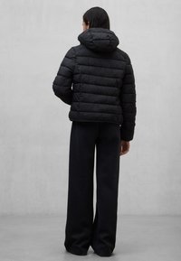 Czarna kurtka puchowa z kapturem, z pikowanymi sekcjami i krótkim krojem, zestawiona z szerokimi czarnymi spodniami na neutralnym tle.