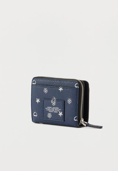 Marineblå læderpung med hvide stjerne- og blomstermønstre, lynlåslukning og et mærke med brandlogo foran. Tekstureret overflade, kompakt design.