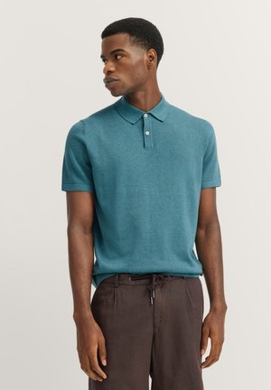 Teal Kurzarm-Polohemd aus strukturiertem Stoff mit klassischem Kragen und Zwei-Knopf-Leiste, kombiniert mit dunkelbraunen Jogginghosen mit Kordelzug.