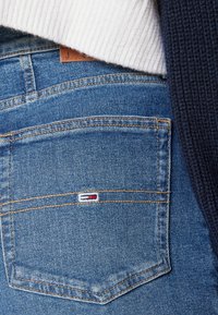 Los pantalones de mezclilla azul cuentan con un bolsillo trasero que tiene una pequeña etiqueta con el logo, mientras que la parte superior incluye una tela texturizada en blanco y azul marino.