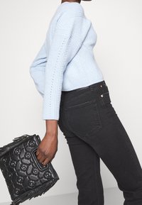 Maglione azzurro chiaro a maglia con texture a coste, abbinato a jeans skinny neri. Borsa nera con motivo in rilievo e dettagli con frange.