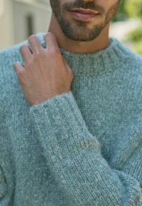 Lyseblå strikket sweater med en struktureret, blød finish. Har en ribbet halsudskæring og manchetter, der fremhæver det hyggelige design.