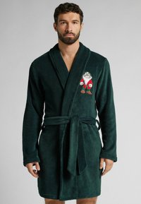 Ciemnozielony, pluszowy szlafrok kąpielowy z długimi rękawami i związaniem w talii, z haftowanym wzorem na piersi.