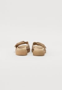Brown slide sandals with a soft texture, featuring a wide strap and flat soles. The design is simple, focusing on comfort and ease of wear.