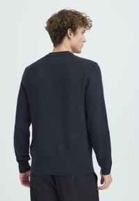 Maglione blu navy scuro realizzato in morbido tessuto a maglia, con colletto rotondo, polsini e orlo a coste, e una vestibilità rilassata. Texture liscia, design semplice.