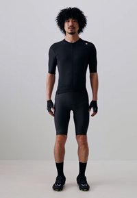 Maglia da ciclismo nera con maniche corte, pantaloni aderenti e guanti. Tessuto liscio e elastico; design minimalista con chiusura a zip.