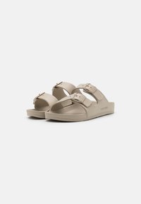 Sandale slip-on bej cu două curele largi, catarame ajustabile, talpă modelată și talpă texturată pentru aderență. Design minimalist fără modele.
