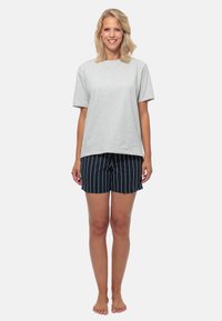 Grijze katoenen T-shirt met korte mouwen, gecombineerd met marineblauwe shorts met witte verticale strepen. Model staat op blote voeten.