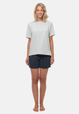 T-shirt grigia in cotone con maniche corte abbinata a pantaloni corti blu navy con strisce verticali bianche. Il modello è in piedi a piedi nudi.