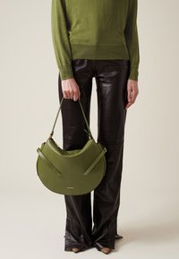 Grüne Lederhandtasche in Halbmondform, mit flachem Körper und zwei verstellbaren Trägern. Merkmale sind goldfarbene Hardware und minimale Markenkennzeichnung.