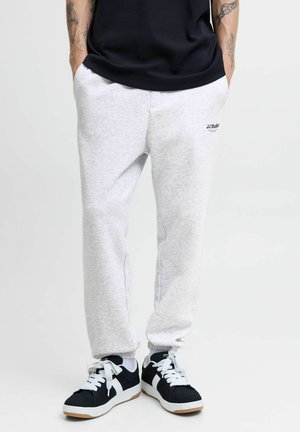 Gray cotton sweatpants with a slim fit, featuring side pockets and a logo accent. Paired with black and white sneakers with laces.