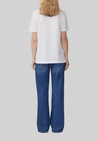 T-shirt en coton blanc à manches courtes associé à un jean en denim bleu à jambe large. Le jean présente un design classique à cinq poches.