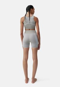 Completo sportivo grigio composto da un reggiseno fitted e pantaloni corti a vita alta. Texture liscia con cuciture a contrasto e un logo discreto sulla schiena.