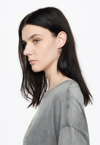 Camiseta gris de gran tamaño con una textura deslavada; presenta un cuello redondo y mangas cortas. Pendientes de aro dorados con un diseño de hoja.