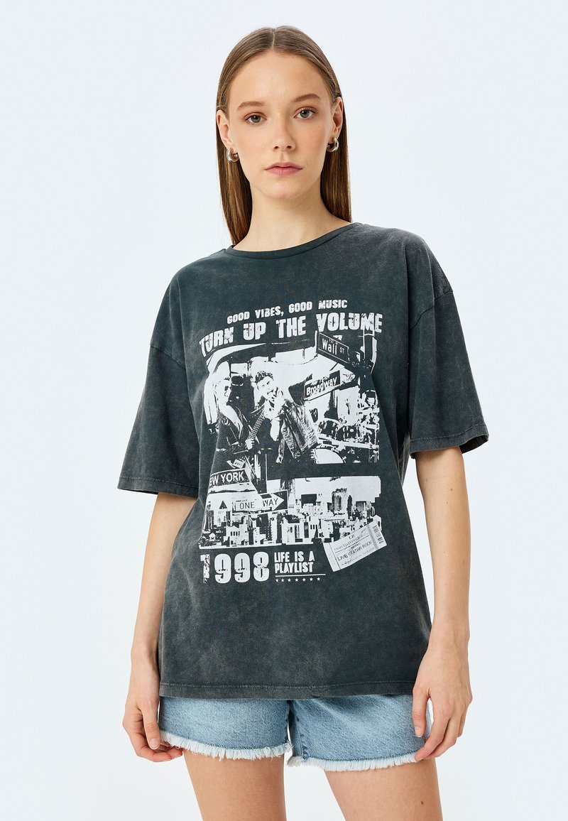 Mørkegrå oversized T-shirt i blød bomuld med en falmet vask. Har grafiske tryk, herunder tekst og billeder af bylandskaber, dateret 1998.