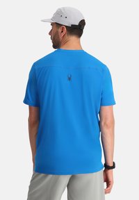 Camisa de hombre de manga corta azul, hecha de una tela ligera, con un logo de araña en la parte posterior, de corte relajado y textura suave.