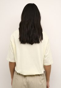 T-shirt en coton crème à manches courtes, coupe décontractée, avec un col rond côtelé, associé à un pantalon beige.