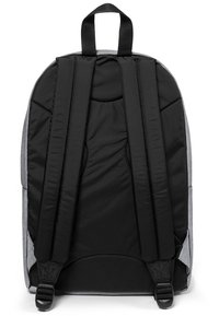 Mochila de tela gris con correas y panel trasero acolchados en negro. Presenta un asa en la parte superior y una textura suave sin patrones visibles.