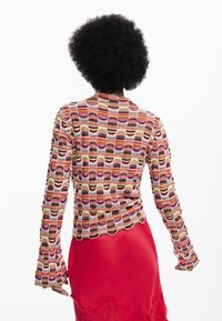 Kolorowa, długorękawowa dzianinowa bluzka z falistym wzorem w odcieniach różu, czerwieni i kremu, o dopasowanym kroju i rozszerzanych mankietach.