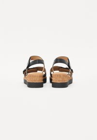 Black sandals with a cork wedge heel and textured rubber sole, featuring adjustable straps and an open back design.