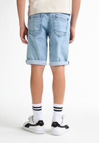 Světle modré džínové kraťasy s ohrnutými manžetami, které mají dvě zadní kapsy a volný střih. Nosené s bílými a černými pruhovanými ponožkami a teniskami.