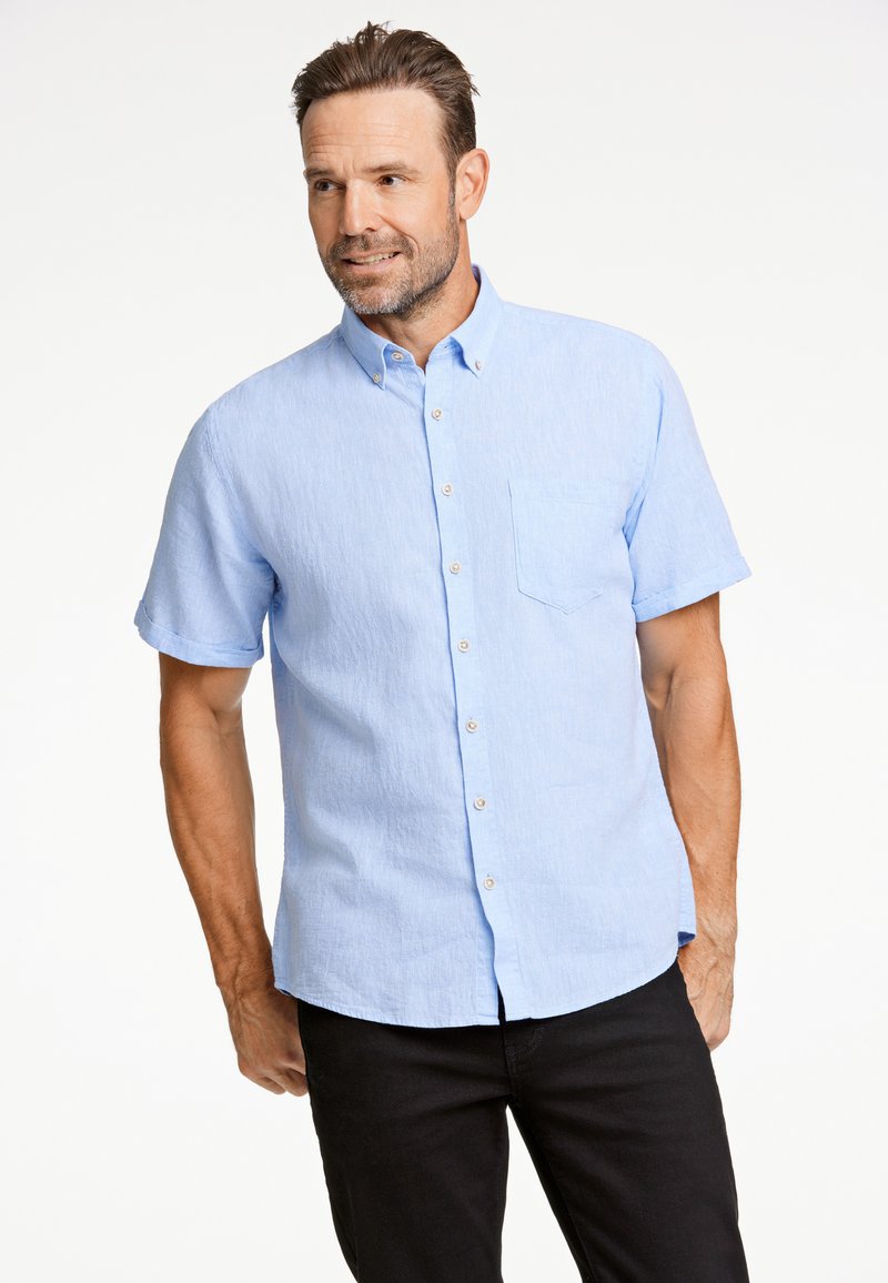 Lyhythihainen, vaaleansininen napillinen paita, joka on valmistettu tekstuurikankaisesta materiaalista. Paidassa on rintatasku ja huomaamattomat napit, ja se on yhdistetty tummiin housuihin.