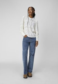 White eyelet blouse with puffed sleeves, paired with blue straight-leg jeans and brown clogs, set against a light gray background.